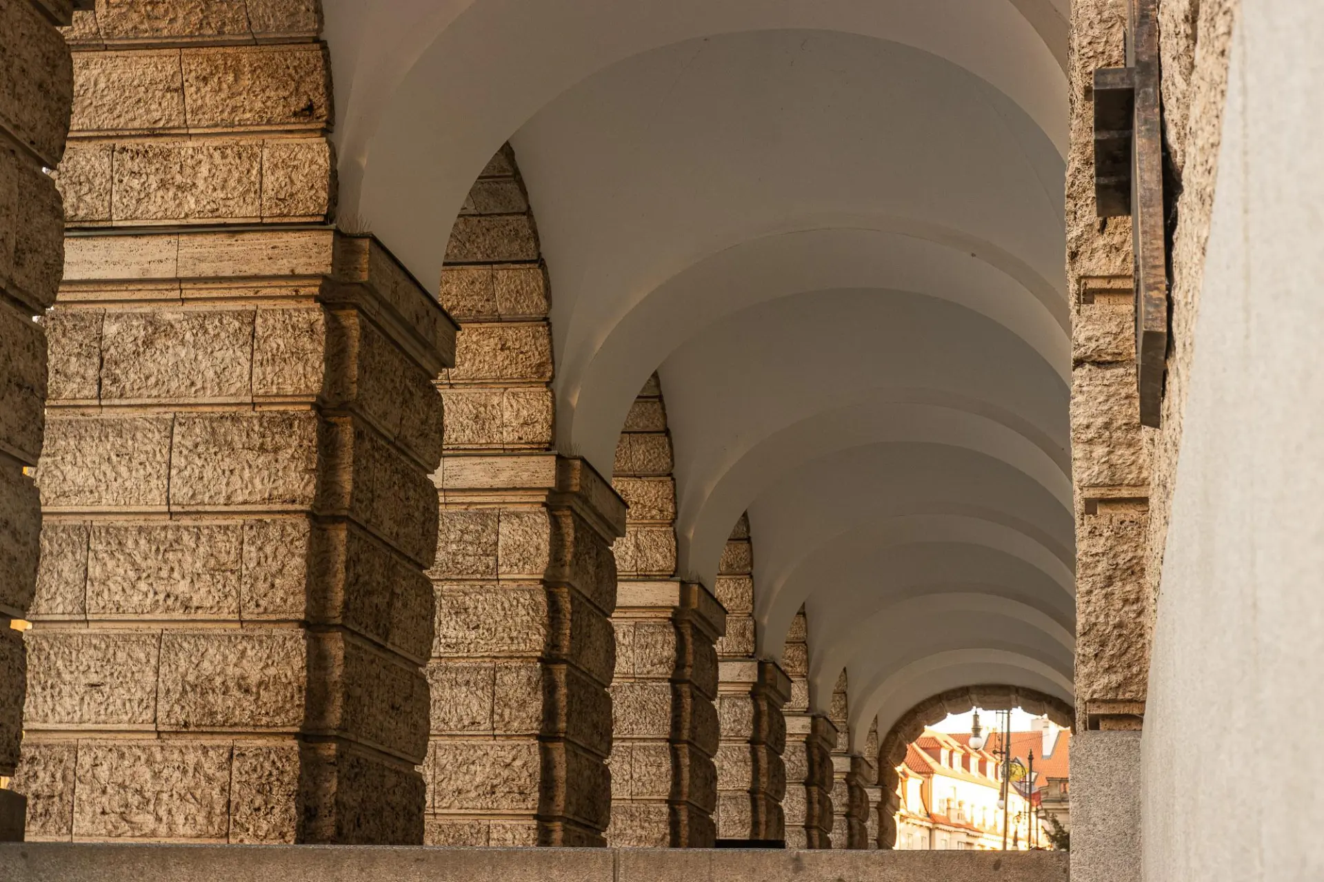 A monumental stone arcade of repeated classical arches receding in perspective toward daylight