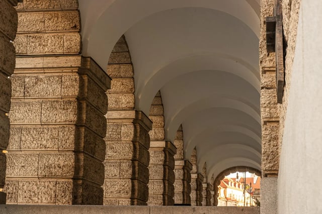 A monumental stone arcade of repeated classical arches receding in perspective toward daylight