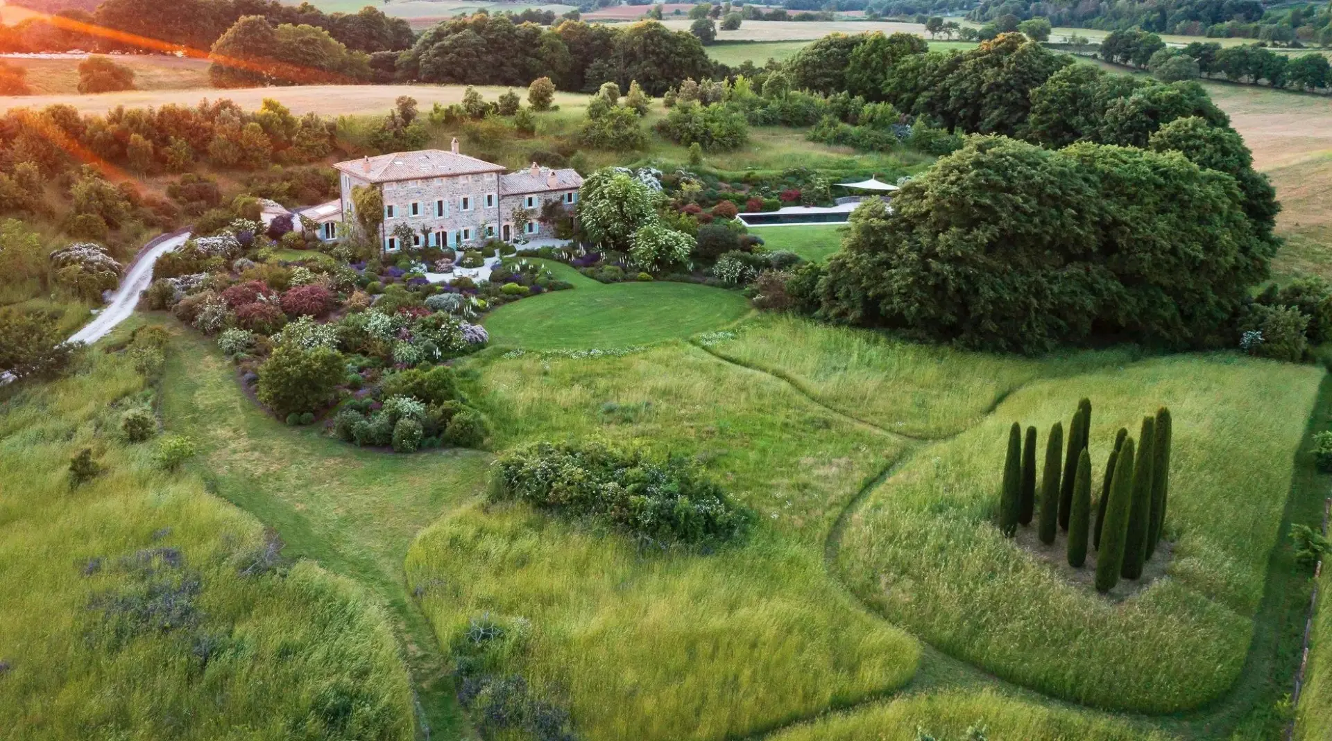 A stone country estate set within extensive gardens and open countryside at sunset