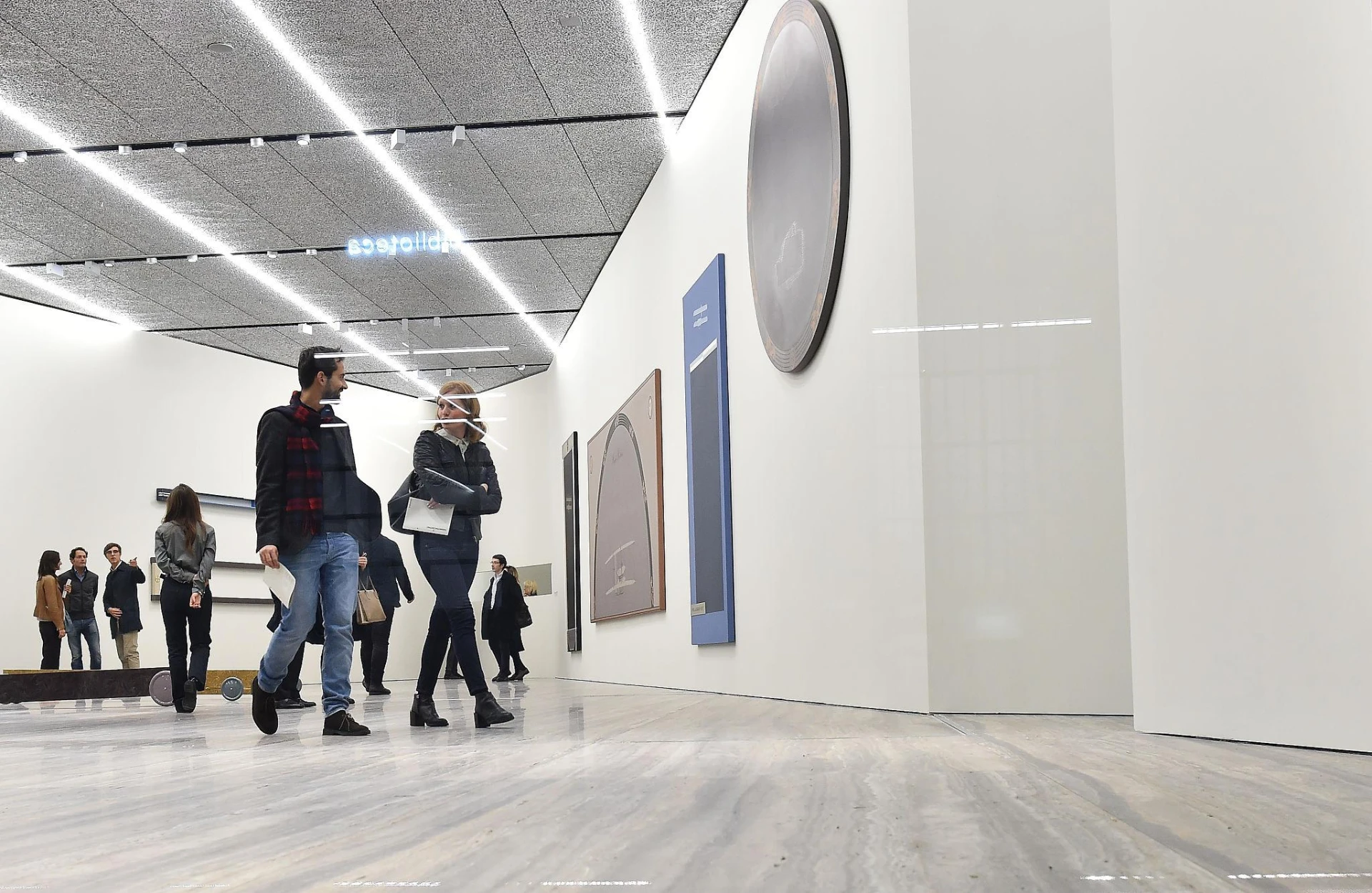 A large architectural interior with strong diagonal light lines and small human figures moving through the space