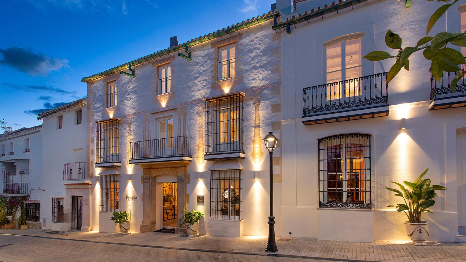 An illuminated historic Mediterranean building façade at blue hour, with wrought-iron balconies and warm interior light